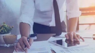 Personne travaillant à un bureau avec des documents, une tablette et un café.
