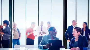 Personnes dans un bureau lumineux discutant près de grandes fenêtres.